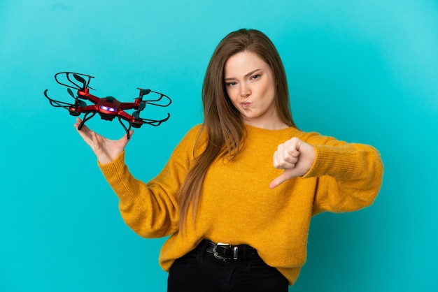 Adolescente tenant un drone sur fond bleu isolé montrant le pouce vers le bas avec une expression négative