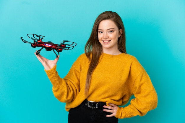 Adolescente tenant un drone sur fond bleu isolé posant avec les bras à la hanche et souriant