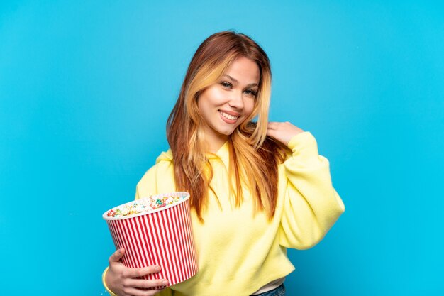 Adolescente tenant des pop-corns sur fond bleu isolé en riant