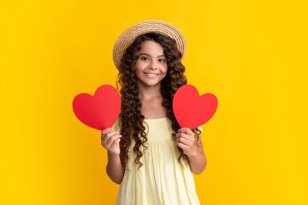 Adolescente tenir forme coeur signe de forme de coeur Enfant tenant un coeur rouge amour vacances Saint Valentin symbole isolé sur fond jaune Heureux adolescent émotions positives et souriantes d'une adolescente