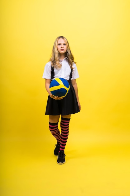 Une adolescente tient un ballon de volley-ball à la main et sourit sur une photo de studio de fond jaune rouge