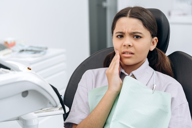 Une adolescente tordue regarde la caméra, touchant sa joue. Une jolie fille noire a mal aux dents