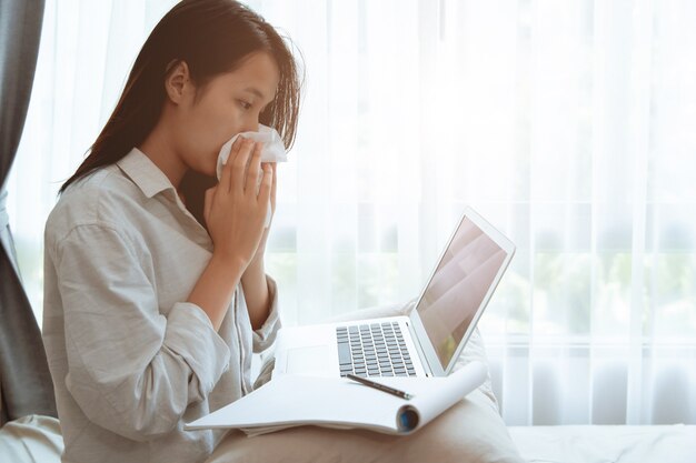 Adolescente en train de s'essuyer le nez lors de l'enseignement à domicile en ligne avec la grippe Coronavirus (Covid-19) infecté, restez à la maison pour travailler avec un ordinateur portable pendant le verrouillage de la ville.