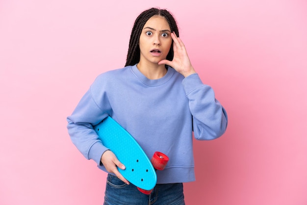 Adolescente avec des tresses sur fond rose isolé avec un patin et faisant un geste surprise