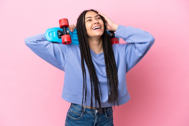 Adolescente avec des tresses sur fond rose isolé avec un patin et levant les yeux