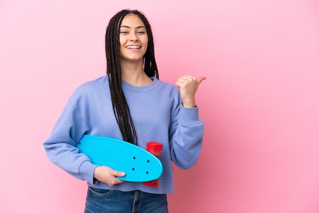 Adolescente avec des tresses sur fond rose isolé avec un patin et pointant vers le côté