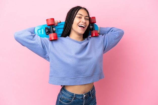 Adolescente avec des tresses sur fond rose isolé avec un patin