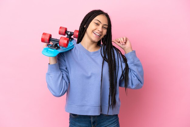 Adolescente avec des tresses sur fond rose isolé avec un patin