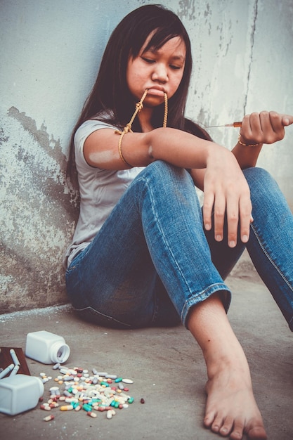 Une adolescente triste avec de la drogue assise sur le sol contre le mur.