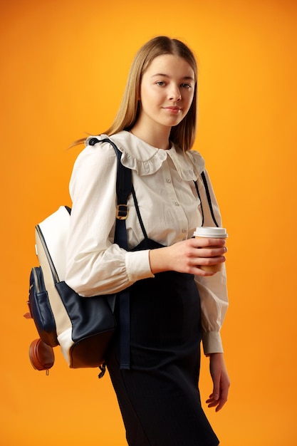 Une adolescente en uniforme scolaire porte un sac à dos sur fond jaune