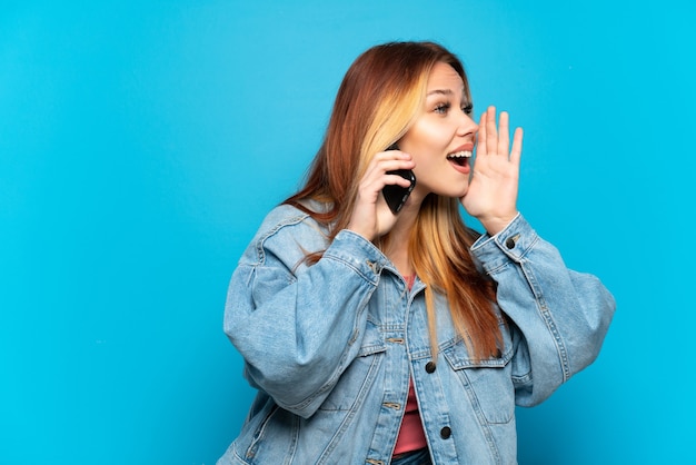 Adolescente utilisant un téléphone portable sur fond isolé criant avec la bouche grande ouverte sur le côté