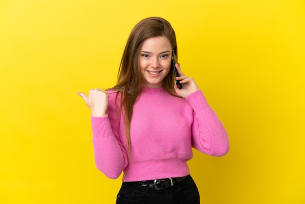 Adolescente utilisant un téléphone portable sur fond jaune isolé dans l'intention de réaliser la solution tout en levant un doigt vers le haut