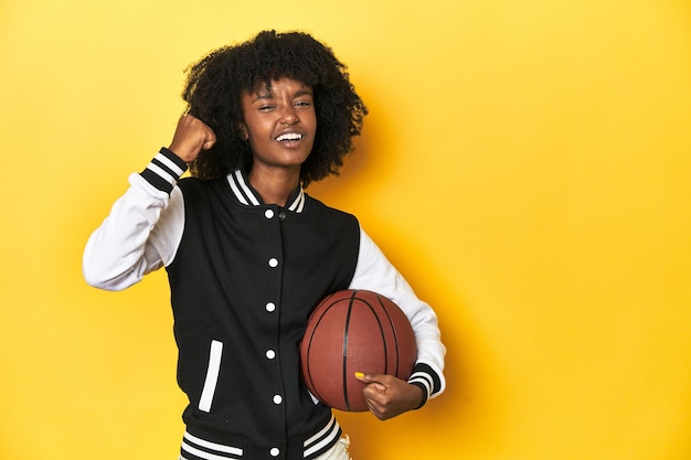 Photo une adolescente vibrante avec un basket-ball sur un fond jaune de studio lève le poing après une victoire.