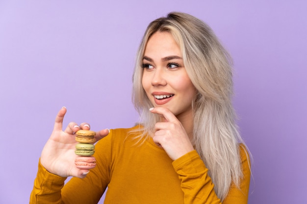 Adolescente sur violet tenant des macarons français colorés et penser une idée