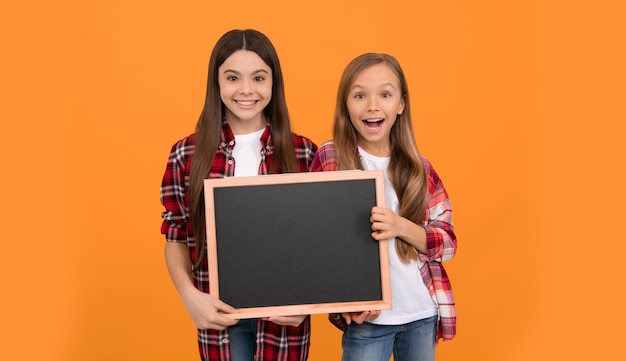 Des adolescentes heureuses tiennent des enfants au tableau noir faisant de la publicité pour la rentrée scolaire des enfants présentant des informations