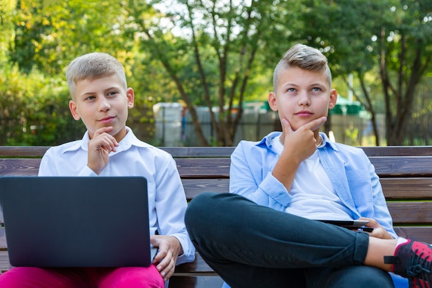 Adolescents sur le banc de parc à l'aide d'un ordinateur portable et d'une tablette numérique