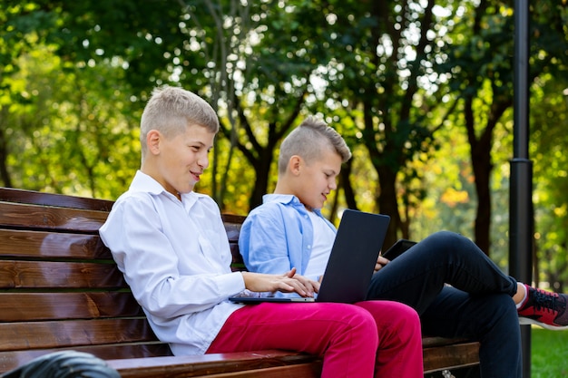 Adolescents sur le banc de parc à l'aide d'un ordinateur portable et d'une tablette numérique