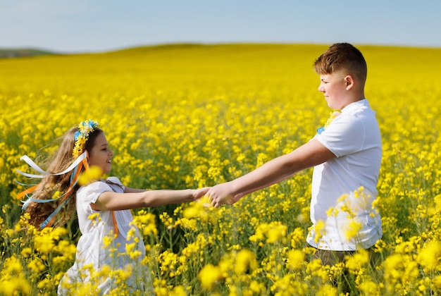 Adolescents frère et sœur avec couronne ukrainienne avec sur la tête dans le champ de colza sous le ciel bleu