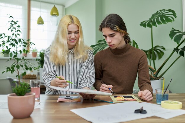 Adolescents gars et fille assis à table avec des dessins de pinceaux de peinture