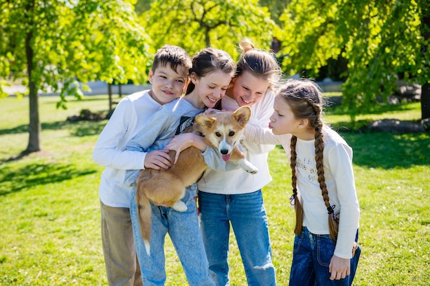 Des adolescents jouent avec un corgi sur une pelouse verte par beau temps