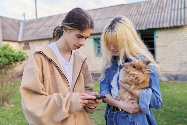 Adolescents avec lapin décoratif dans les mains parlant et regardant un smartphone