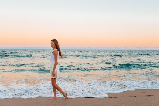 Adorable adolescente en blanc au bord de la mer pendant ses vacances d'été à la plage avec un ciel incroyable sur bac