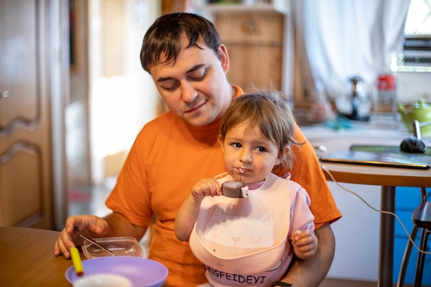 Un adorable bambin aime manger de la crème glacée sur les genoux de ses parents