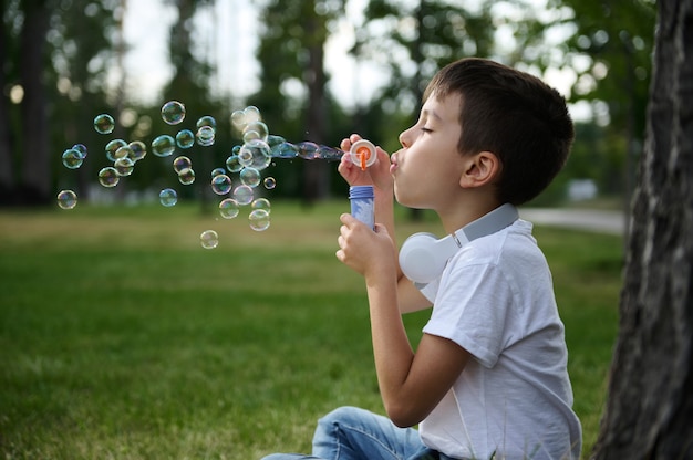 Adorable beau garçon préadolescent soufflant des bulles de savon sur le parc, se reposant pendant ses loisirs à l'école