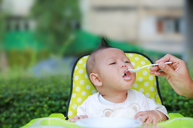 Adorable bébé garçon assis sur la chaise et manger de la nourriture pour la première fois.