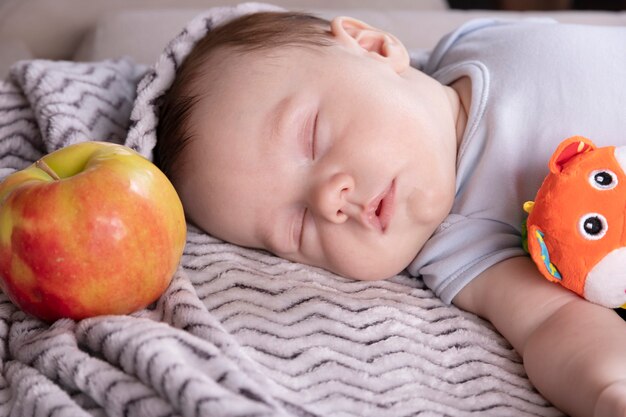 Adorable bébé, jouet préféré, pomme rouge, sommeil détendu et allongé sur le lit des parents