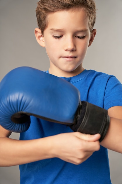 Photo adorable boxeur enfant mâle serrant le gant de boxe autour du poignet avant la pratique