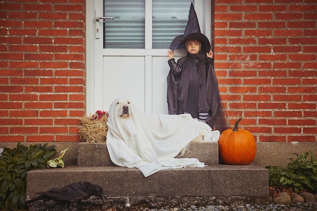 Adorable enfant avec un chien sur le porche vêtu de costumes d'halloween.