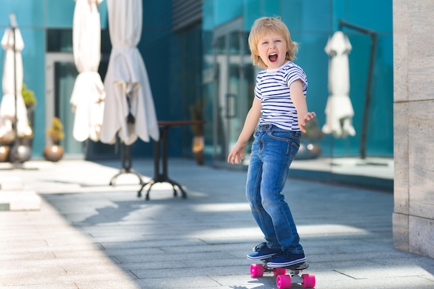 Adorable enfant à l'extérieur. Joli joli enfant souriant à la caméra. Garçon décontracté sur l'heure d'été patiner sur une planche à roulettes.