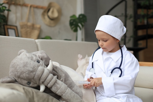 Adorable enfant habillé en médecin jouant avec un éléphant jouet, vérifiant son souffle avec un stéthoscope.