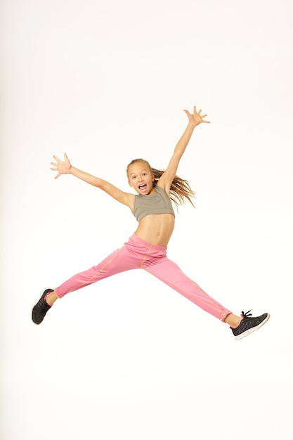 Adorable enfant de sexe féminin en tenue de sport sautant en l'air et levant les bras. Isolé sur fond blanc