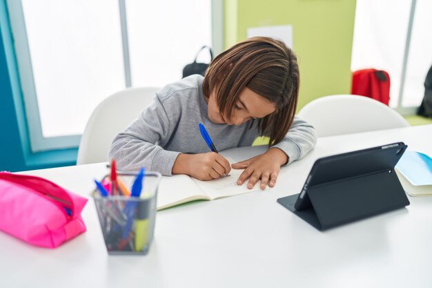 Adorable étudiant hispanique assis sur une table à faire ses devoirs en classe