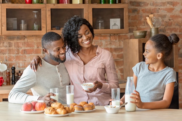 Adorable famille africaine de trois personnes prenant le petit déjeuner dans la cuisine, mangeant et parlant, espace de copie