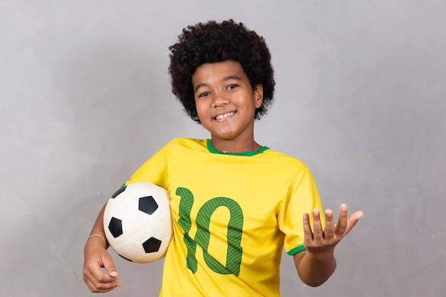 Photo adorable fan brésilien de garçon afro tenant un ballon de football