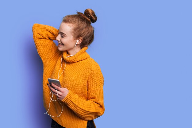 Adorable femme aux cheveux rouges et taches de rousseur écoute de la musique sur un mur de studio bleu avec espace libre