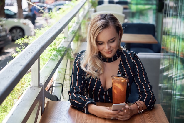 Adorable femme blonde à l'aide de smartphone assis sur la terrasse