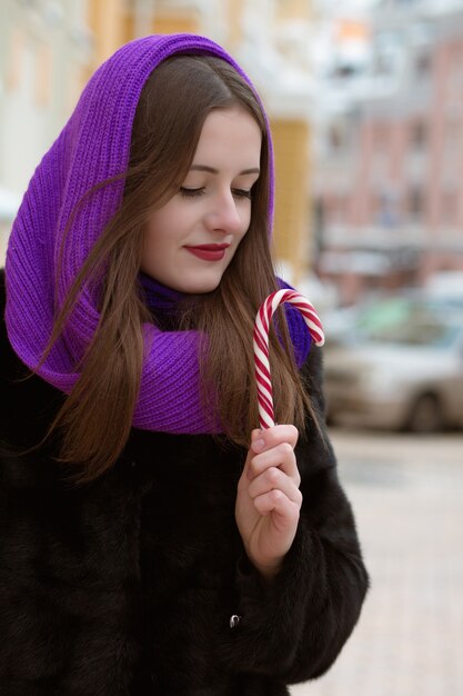 Adorable femme brune tenant une canne en bonbon au caramel dans la rue