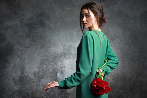 Adorable femme portant une robe élégante tenant une fleur de pivoine rouge