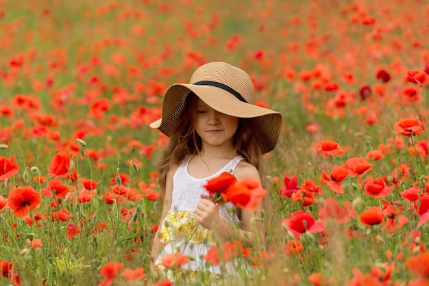 Adorable fille de 6 ans dans un champ de coquelicots lumineux Portrait d'une jolie fille aux longs cheveux bouclés contre le champ d'été plein de coquelicots rouges