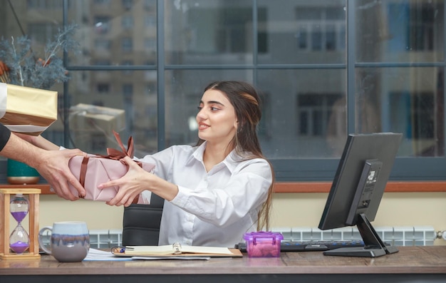 Adorable fille assise au bureau et prenant la boîte cadeau de quelqu'un