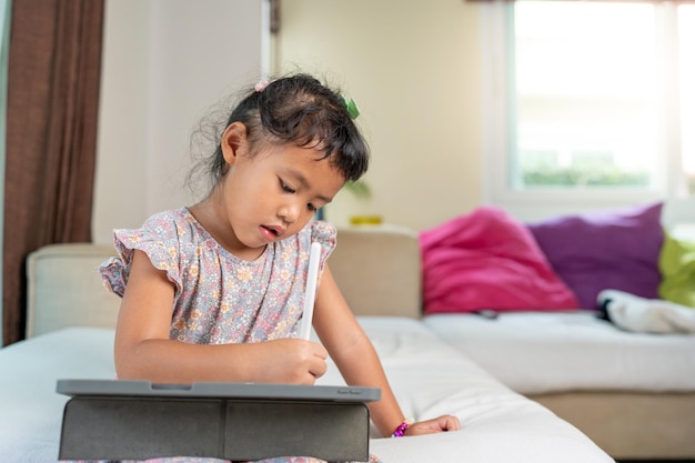 Adorable fille assise sur un canapé à l'aide d'une tablette à la maison Concept d'apprentissage à domicile