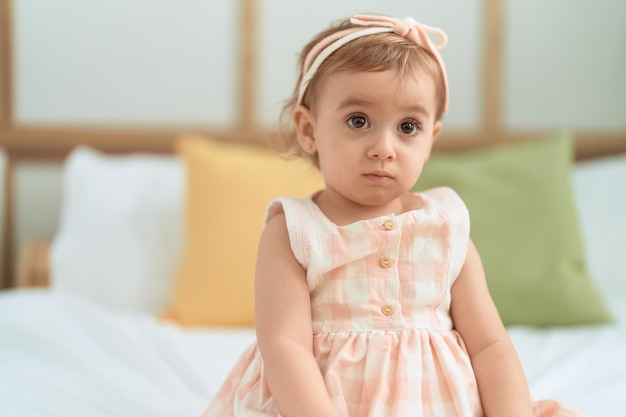 Adorable fille caucasienne assise sur le lit avec une expression détendue dans la chambre