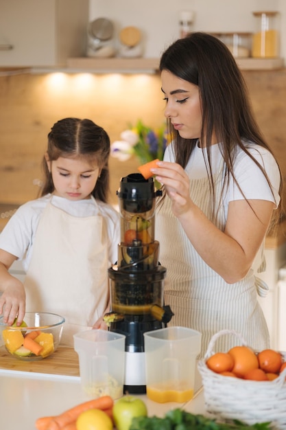 Adorable fille de cinq ans mettant avec sa mère des fruits dans le jus deux femelles dans des tabliers