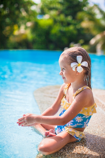 Adorable fille avec une fleur derrière son oreille se trouve près de la piscine