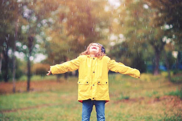 Adorable fille en manteau de pluie jaune jouant sous la pluie dans le parc en automne