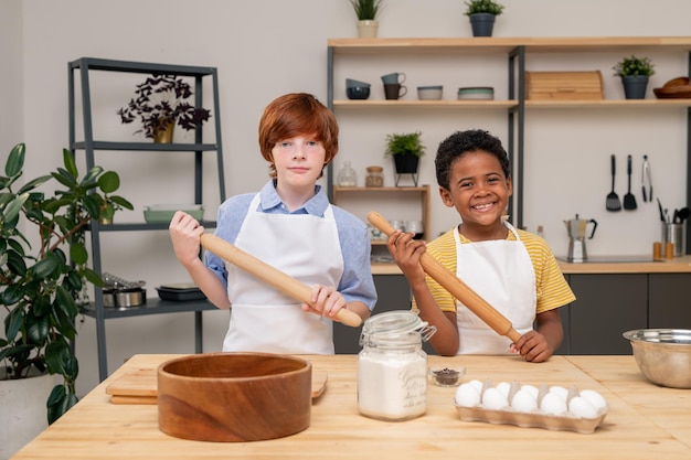 Adorable fille portant un tablier regardant la caméra avec un large sourire tout en regardant une émission de télévision sur la cuisine sur une tablette numérique afin de préparer une salade appétissante pour sa famille, portrait